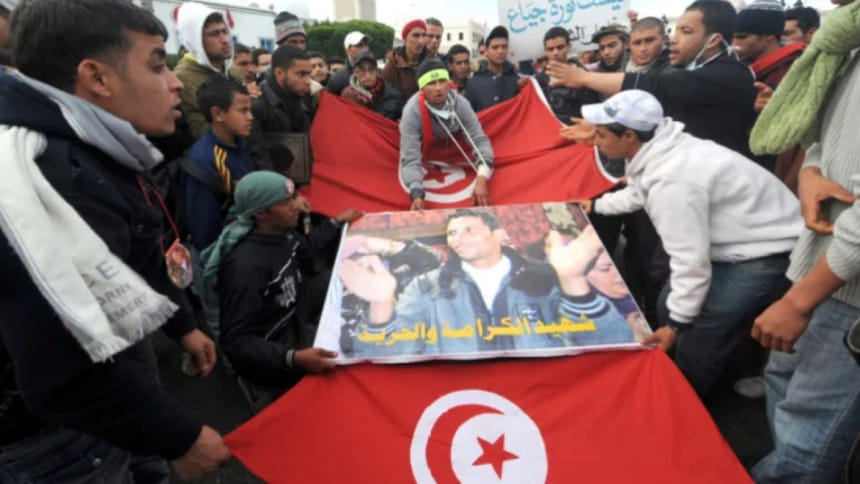 ‘আরব বসন্ত’ আন্দোলনের পথিকৃত মোহাম্মদ বোয়াজিজি’র পোস্টার ও তিউনিসিয়ার পতাকা হাতে ক্যাসেরিন অঞ্চলের মানুষ সরকারী রাজপ্রাসাদের সামনে বিক্ষোভ করছেন। ফাইল ছবি: এএফপি (২৮ জানুয়ারি, ২০১১)   