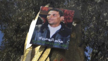 তিউনিসিয়ার সিদি বৌজিদ এলাকায় মোহাম্মদ বোয়াজিজির ছবি যুক্ত পোস্টারের সামনে তরুণ-তরুণীরা জমায়েত হয়। বোয়াজিজির মৃত্যুতে দেশটিতে সরকারবিরোধী বিক্ষোভ শুরু হয়, যা সমগ্র মধ্যপ্রাচ্যে ছড়িয়ে পড়ে। ফাইল ছবি: ডয়চে ভেলে (১৯ জানুয়ারি, ২০১১)  